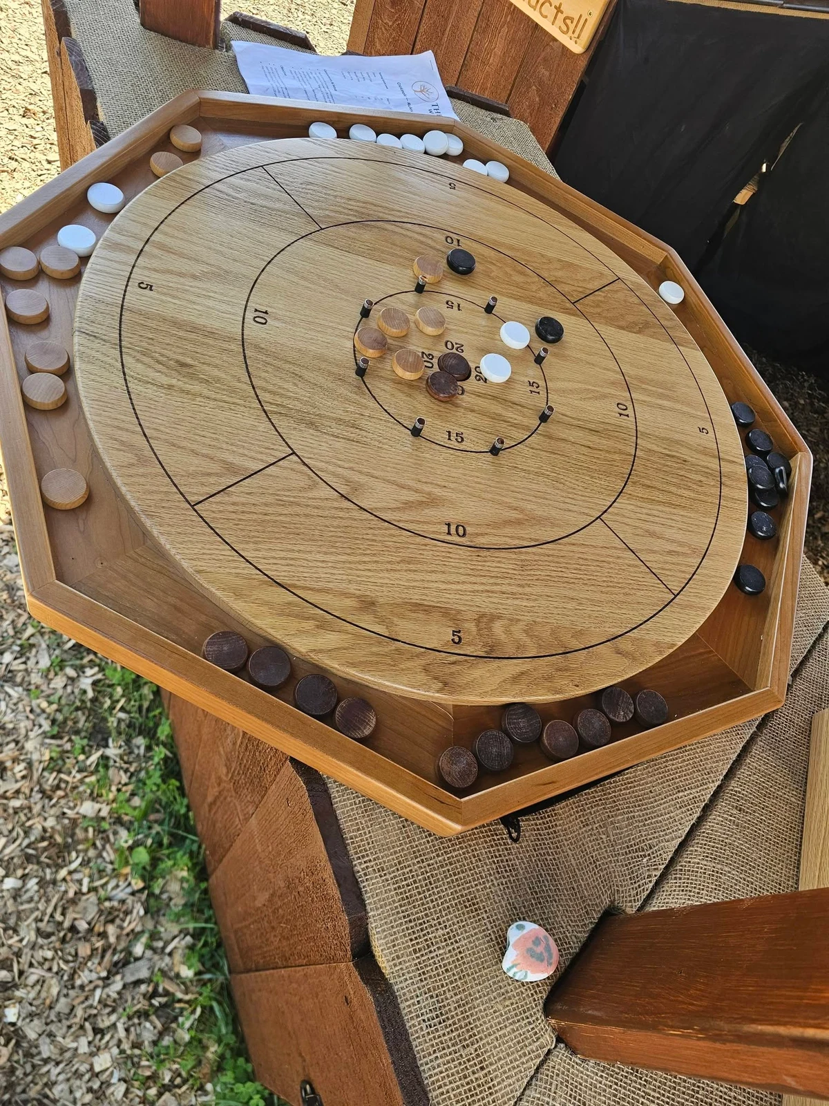 A wooden Crokinole board with scoring rings, pegs and playing discs.